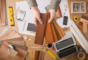 10 Good Reasons to choose Hancock Kitchen and Bath. Professional interior designer holding wood swatches for baseboard and skirting, hands close up with desktop on background